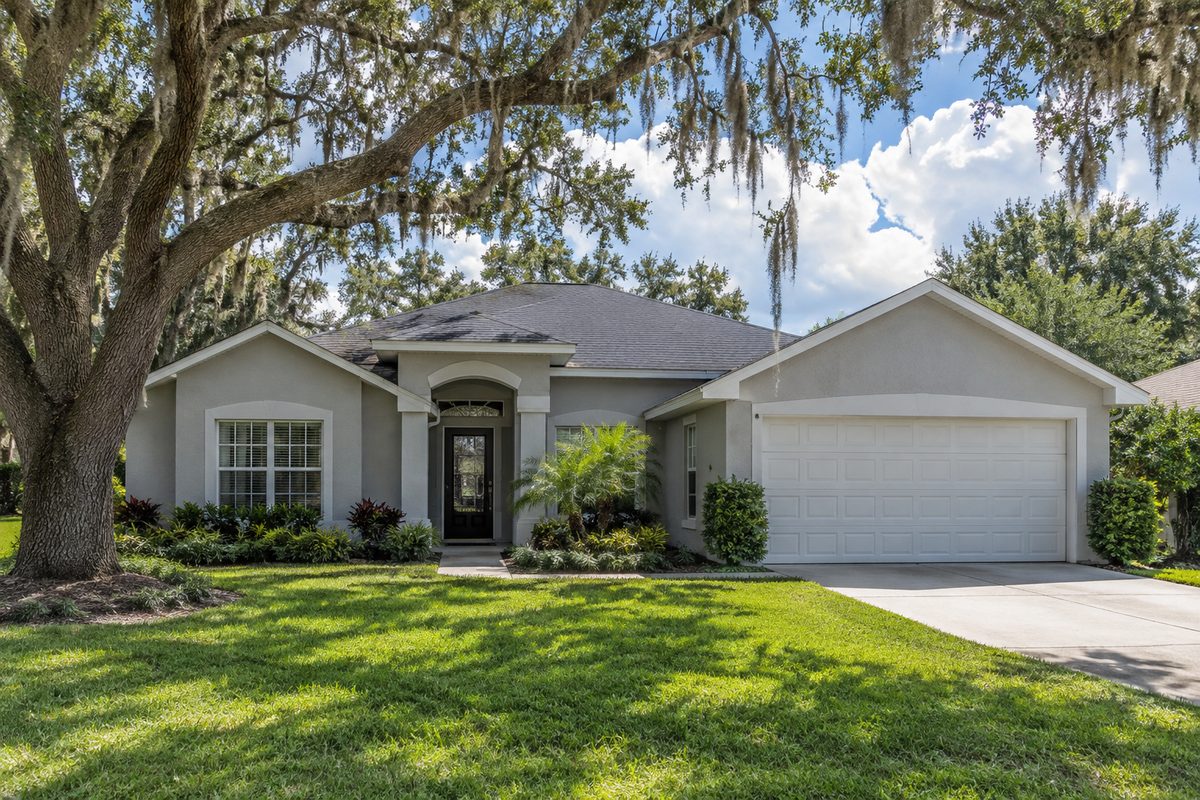 Suburban Orlando home with grey stucco, live oaks with Spanish moss and a white two-car garage door